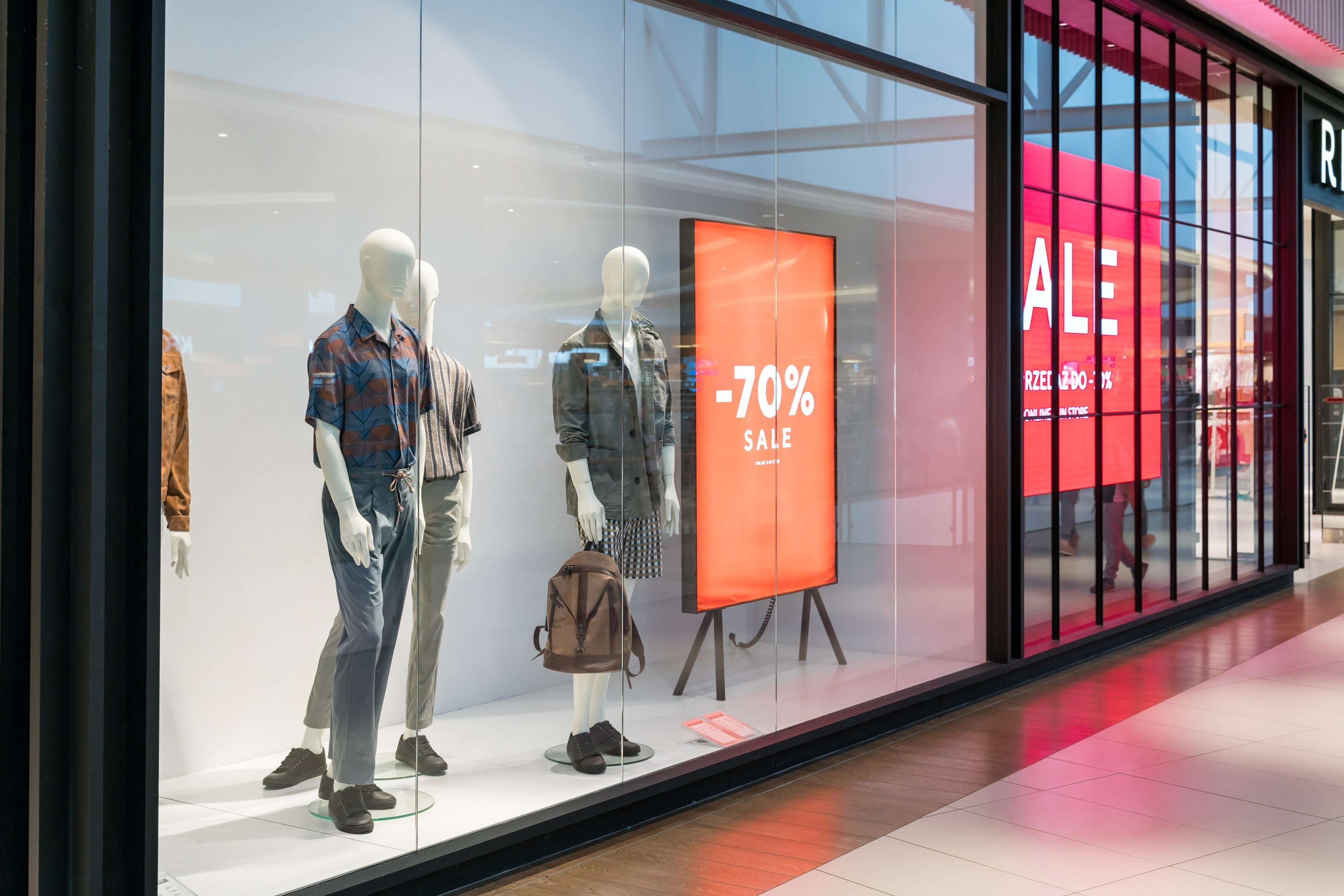 A view of a retail storefront featuring mannequins dressed in stylish clothing. The scene is set in a brightly lit indoor location, possibly a shopping mall.