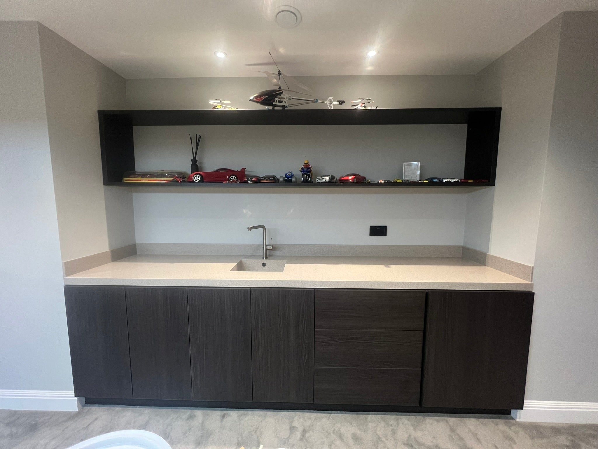 Completed bespoke home bar with dark wood cabinetry, integrated appliances, built-in sink and solid-surface worktop.